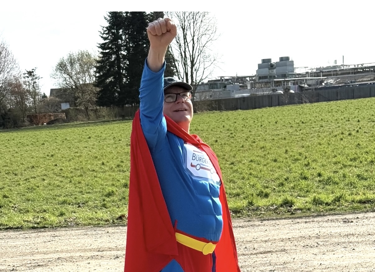 BürgerBus-Unterstützer im blauen Superheldenkostüm mit rotem Umhang und erhobenem Arm