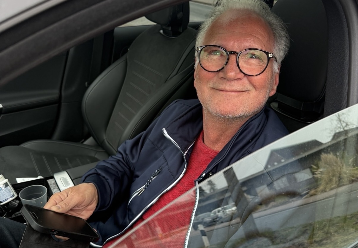 Ein lächelnder Mann mit Brille sitzt am geöffneten Fenster eines Fahrzeugs